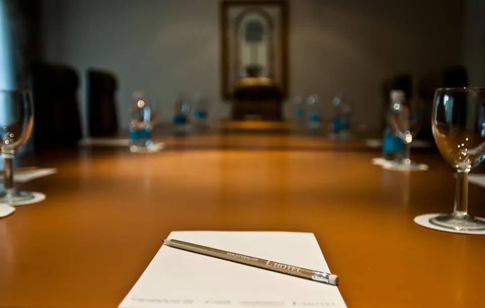 Parlak bir toplantı masasının yakın çekimi; ön planda boş not kâğıdı ve kurşun kalem