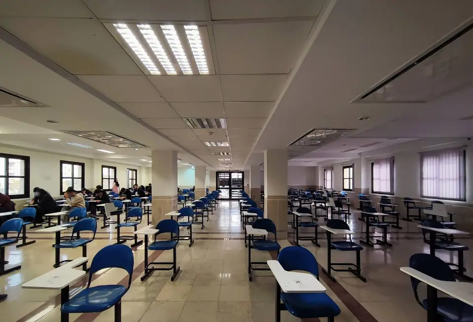 Mavi sandalyeli, tek kişilik sıraların aralıklı dizildiği geniş ve aydınlık bir sınav salonu